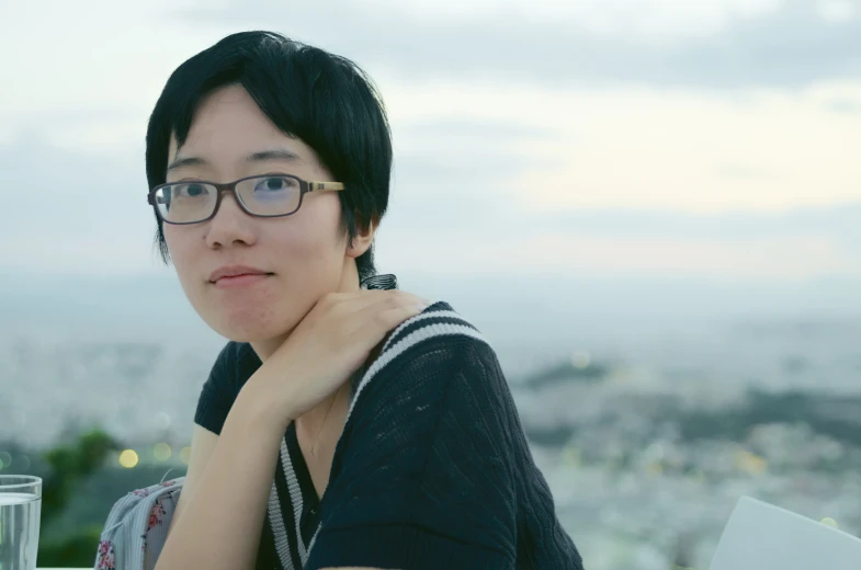 a woman with glasses standing by a tall building