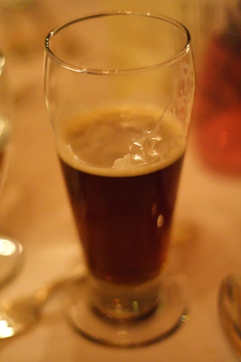 a glass of beer on a plate next to silver ware