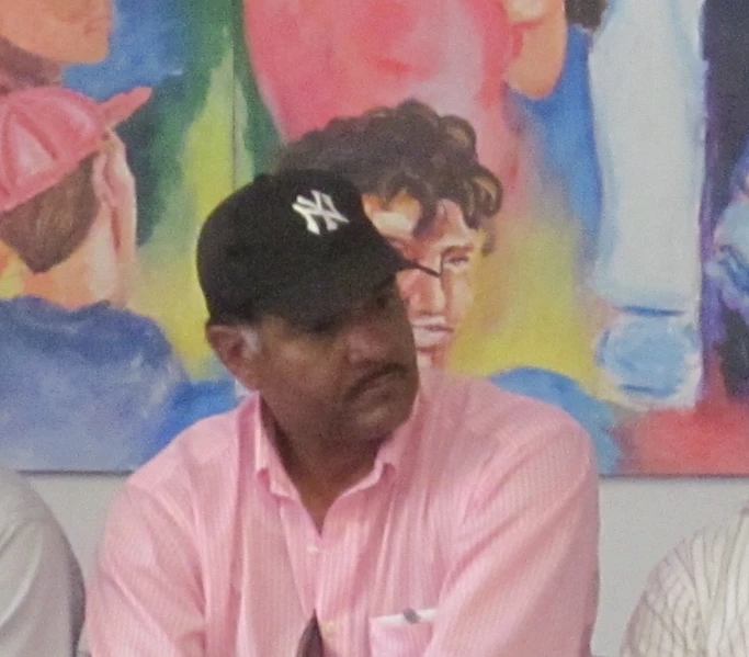 a man with a baseball cap sitting next to two men in front of some paintings