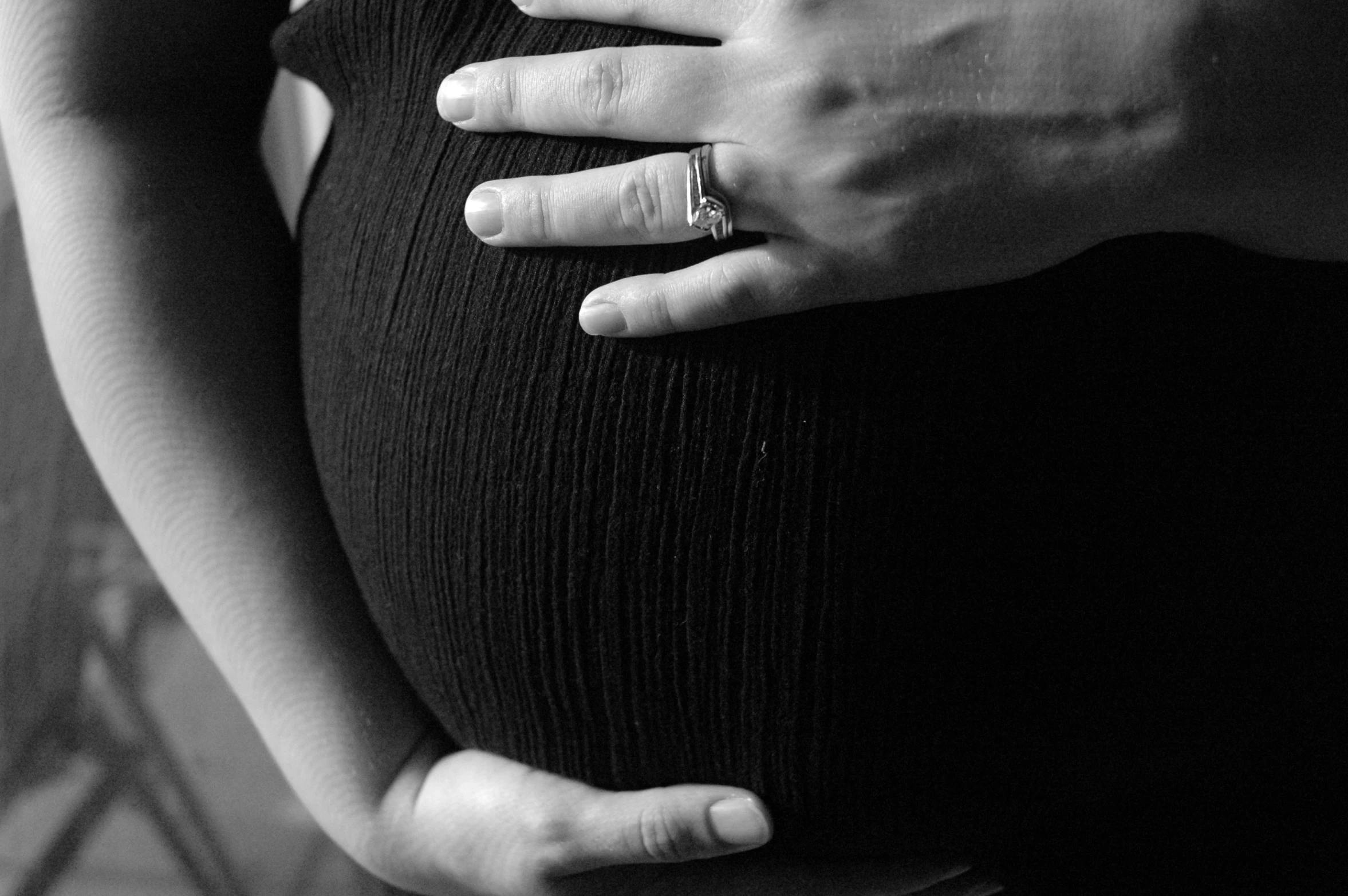 pregnant couple wearing wedding bands and holding hands on belly