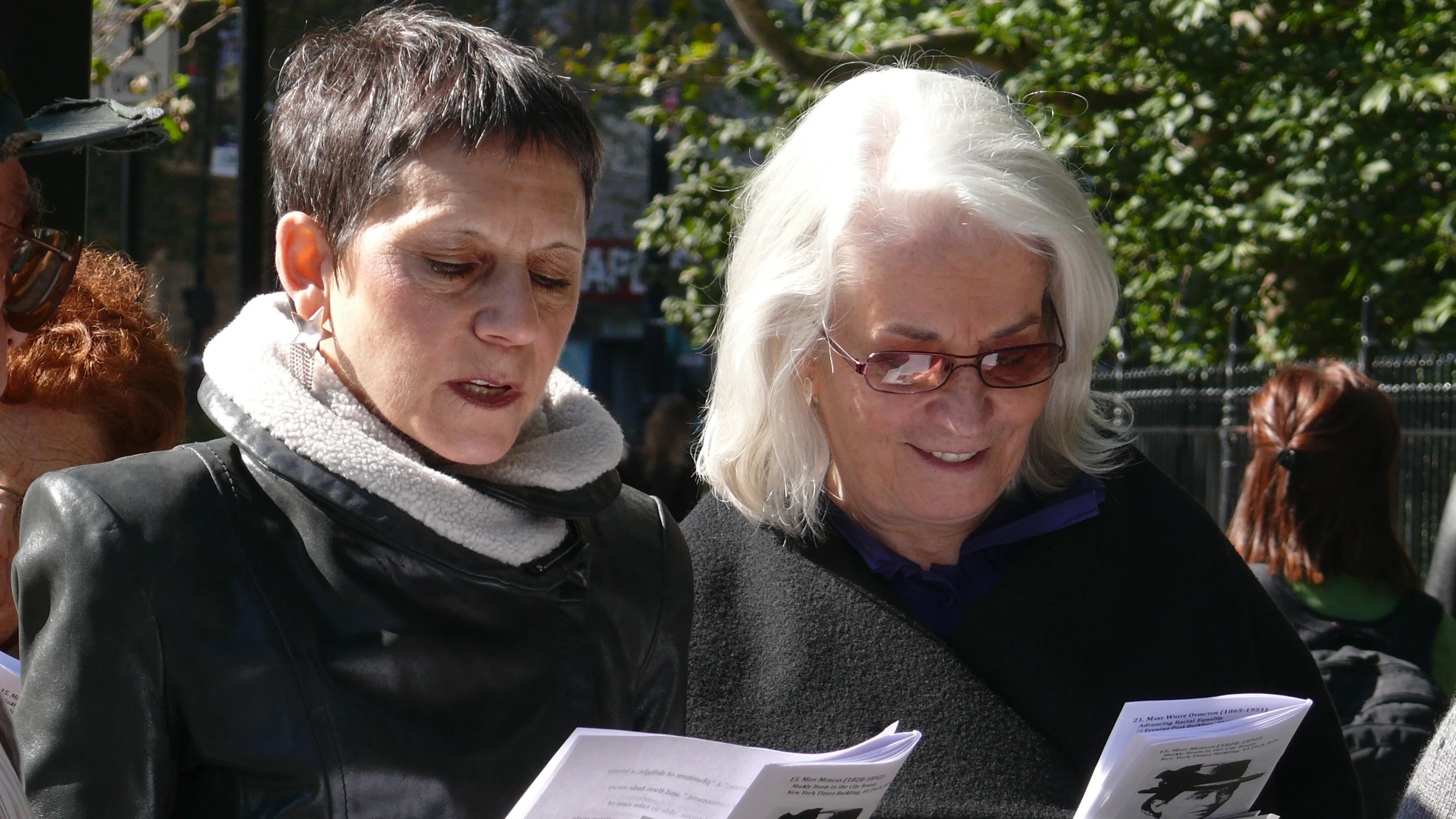 two women stand and read books at an event