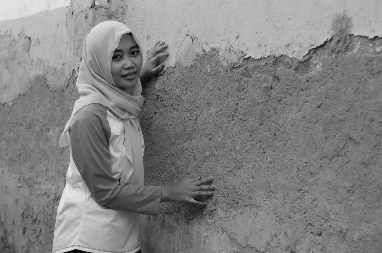a young woman posing for the camera with her hand over a wall