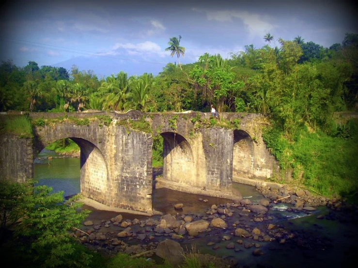 a small stone bridge spanning a river near some green trees