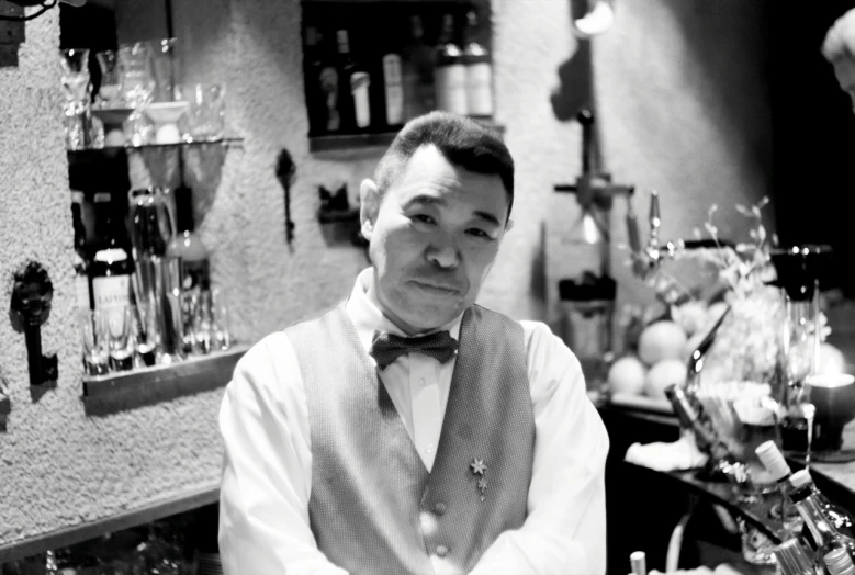 a man with a bow tie and vest standing next to the counter