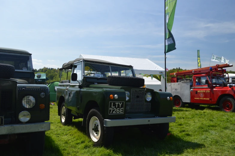 two green trucks parked in a field next to other vehicles