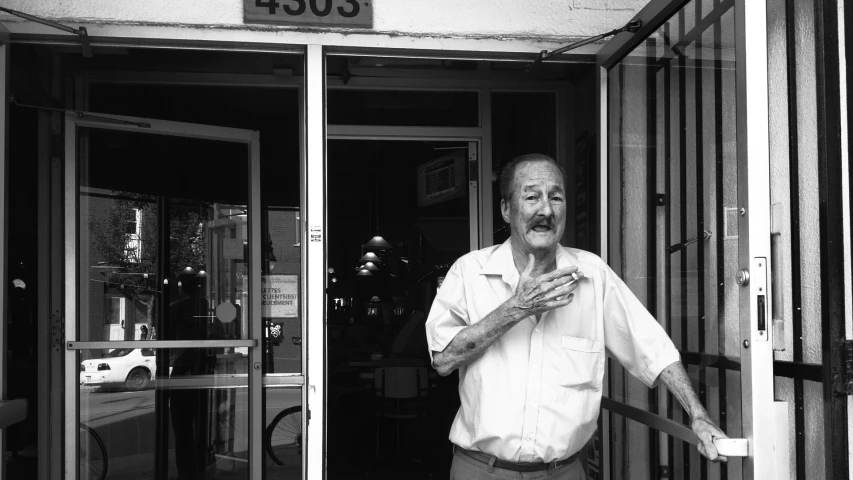 a man with his hands folded standing in front of an open door