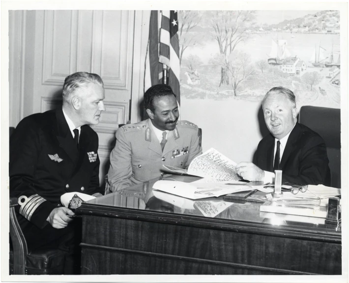 three men in military uniforms are sitting around a desk
