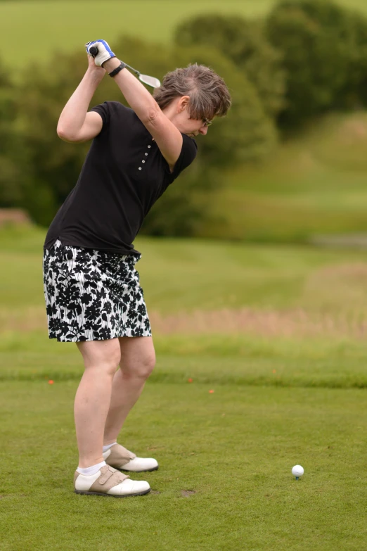 an older woman swinging her golf club at a ball