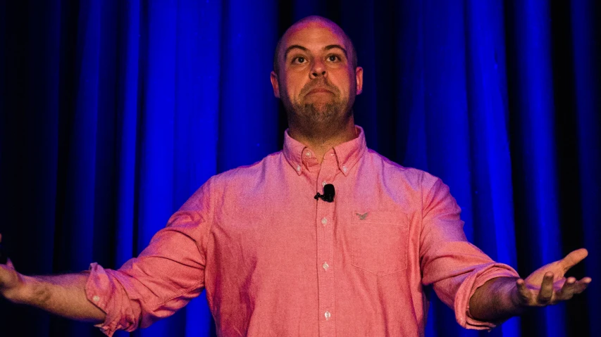 a man in a pink shirt standing on stage with his hands out