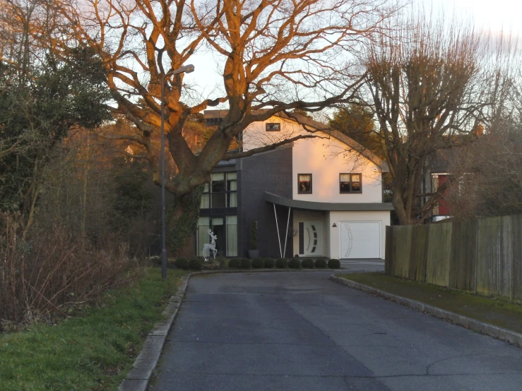 a house on a tree - lined street and a fence