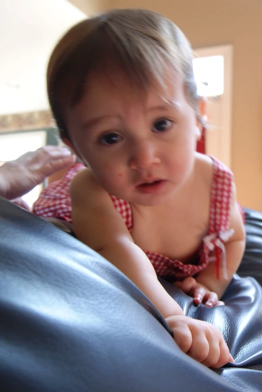 baby in dress is on a couch with a blue comforter