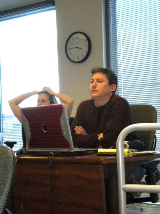 two women at a desk with a clock and a window in the background