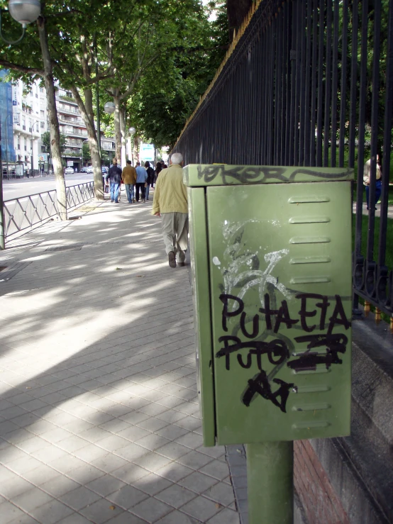 green sign with graffiti on it next to a fence