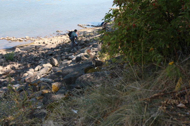 two people standing on a rocky shoreline near the water