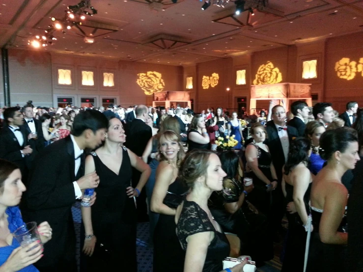 an array of people in formal wear walking through a hall