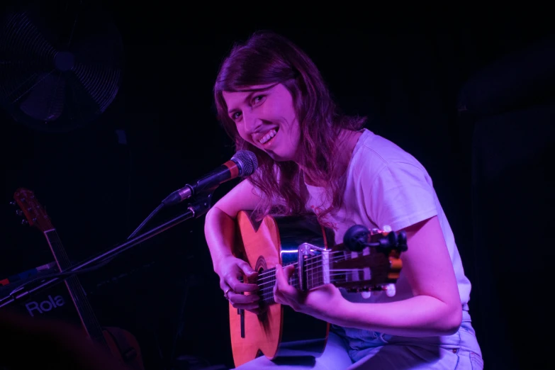 a smiling young lady sitting at the keyboard playing a guitar