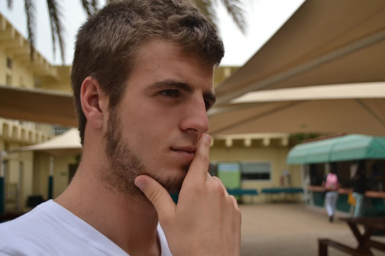 the young man with a hand under his nose is posing for the camera