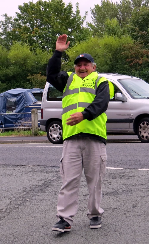 a man in a yellow vest standing on a parking lot with his arm up in the air