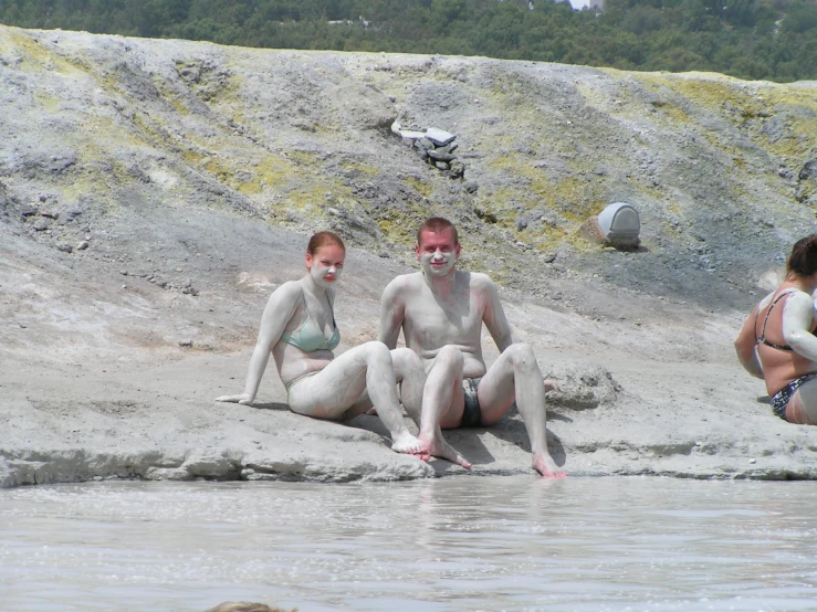 some young people sitting on the side of a body of water