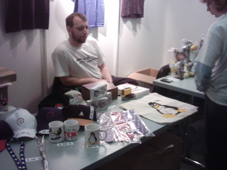 the man is sitting at a table covered with paper, sewing supplies and gifts