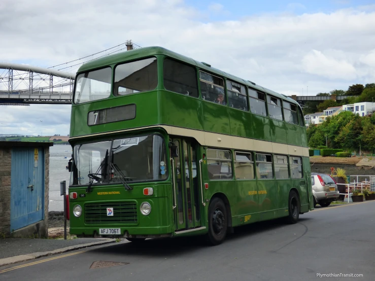 a green bus on the road with a bridge in the background