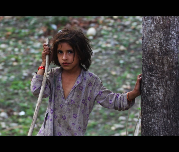 girl in a purple dress leaning against a tree