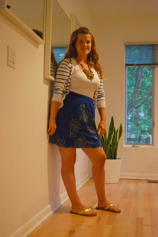 a young lady in a blue and white skirt leans against a wall