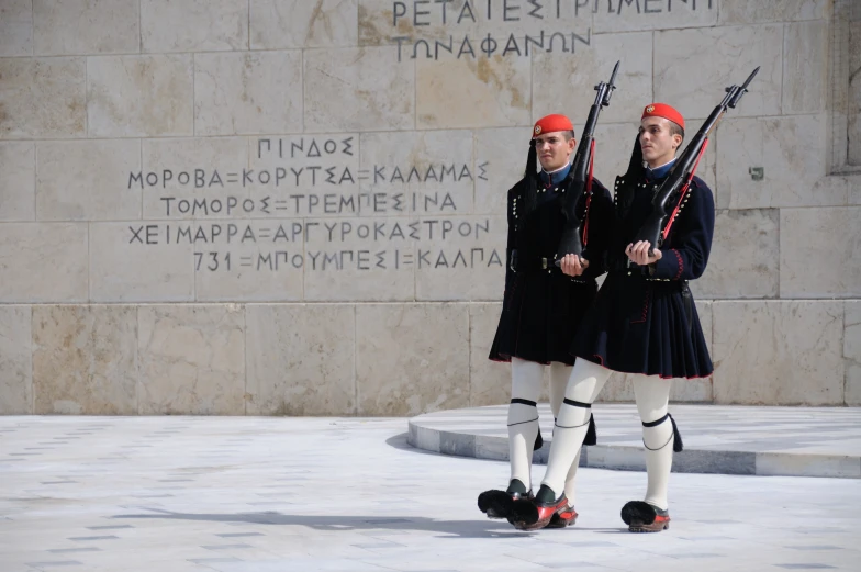 two men in uniforms standing with guns near a wall