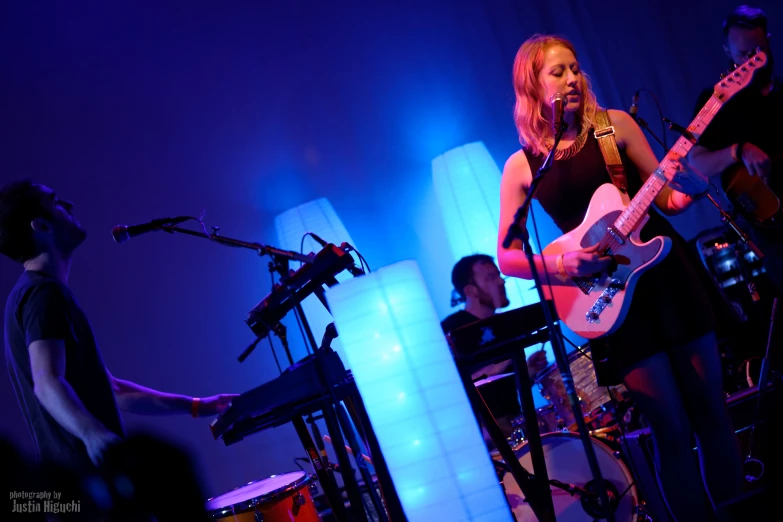 a woman holding a guitar and singing in front of a microphone