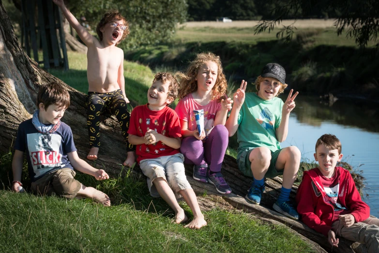 children sitting on a tree by water waving and posing