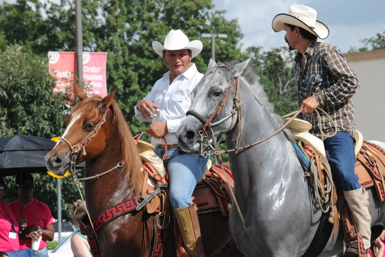 two men on horses wearing hats with people in the background