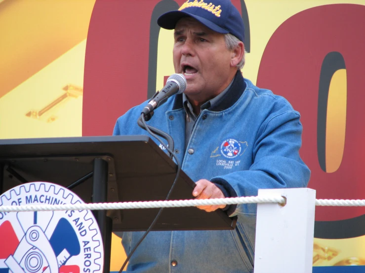 man at podium holding microphone giving speech at outdoor event