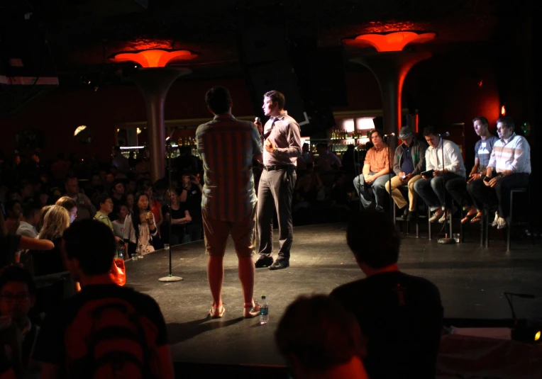 three people speaking and standing on stage with audience watching