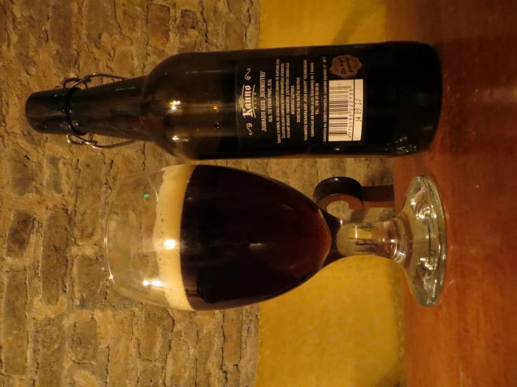 a dark liquid in a beer glass next to a brown bottle