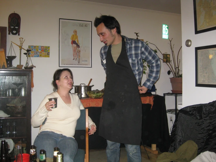 a man and woman standing in a kitchen, drinking wine