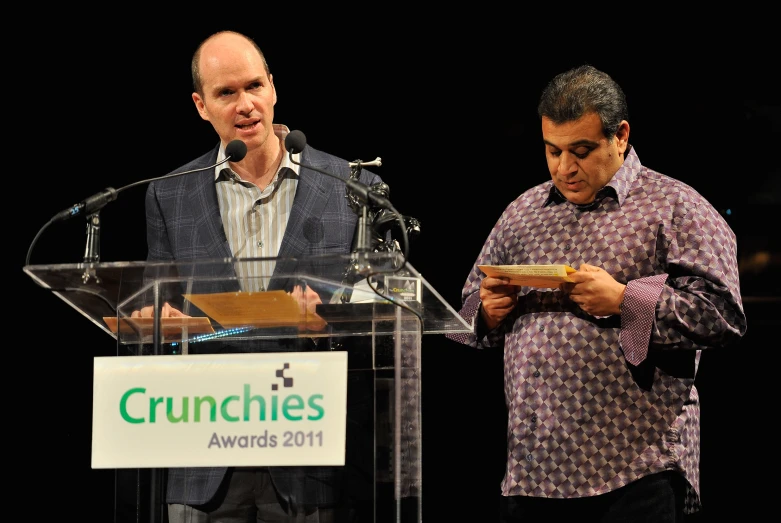 two men standing at a podium, one holding an item and the other reading