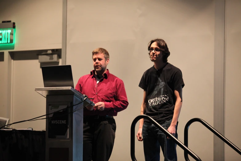 two men speaking at podium with one man standing