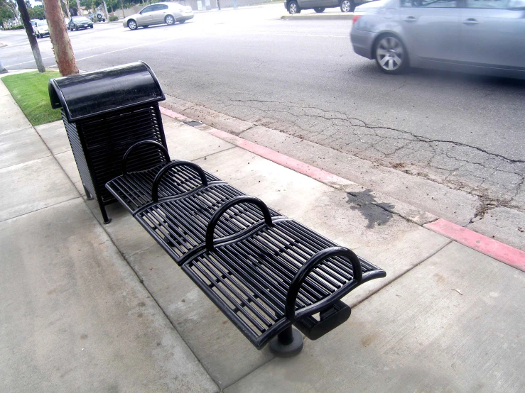 an empty black metal park bench on the side of the street