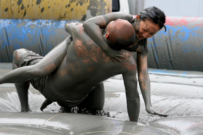 woman in mud covered body wrestling with another woman