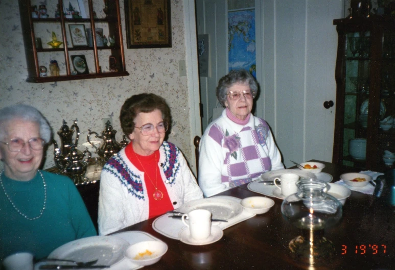 three elderly women are sitting at a table with dishes and coffee