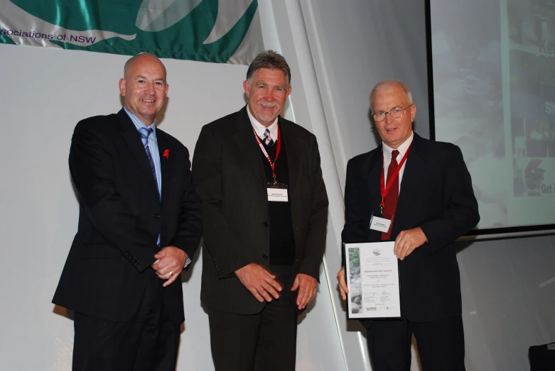 three men in suits standing together in front of a projector screen