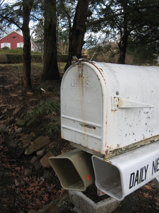 a dirty white mailbox is in the grass near a tree