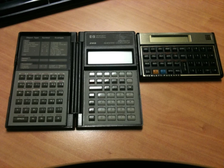 three small black calculators sitting on a wooden table