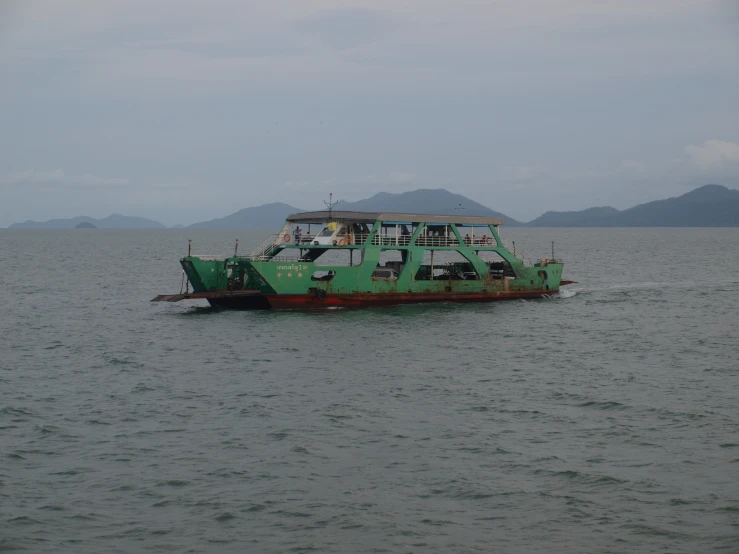 large green boat floating in the ocean on cloudy day