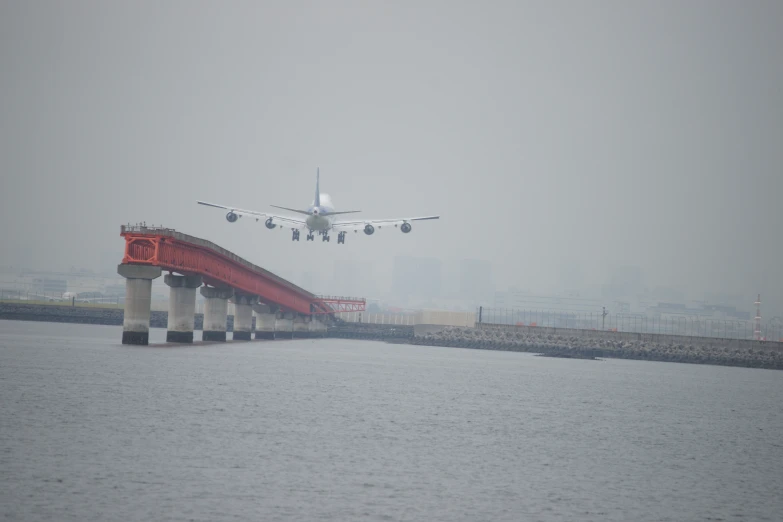 an airplane flying over water with a bridge in the foreground