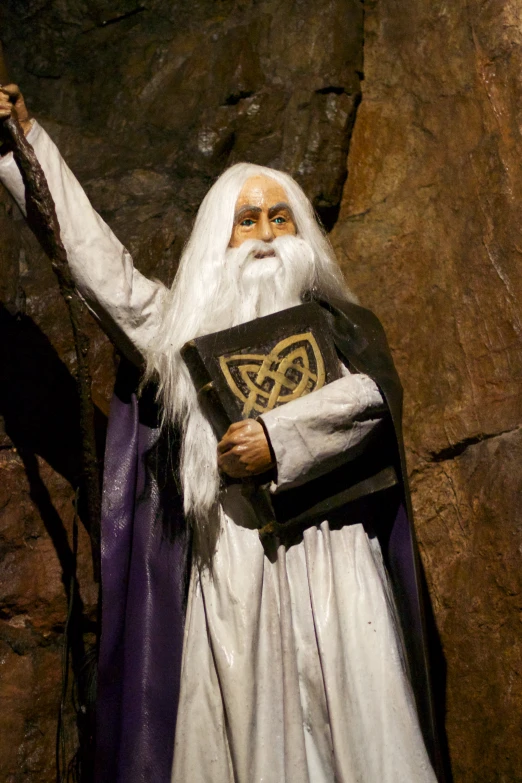a statue with white hair and beard wearing a purple mantle holding a bible