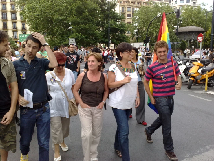 some people standing on the side of the street and one is holding a rainbow flag