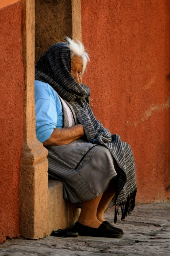 an elderly woman is sitting against a wall