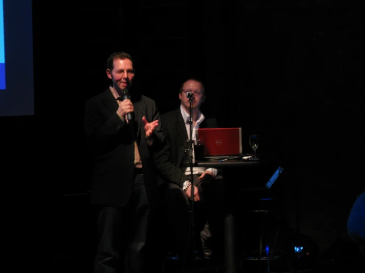 two men are talking on stage with their computers