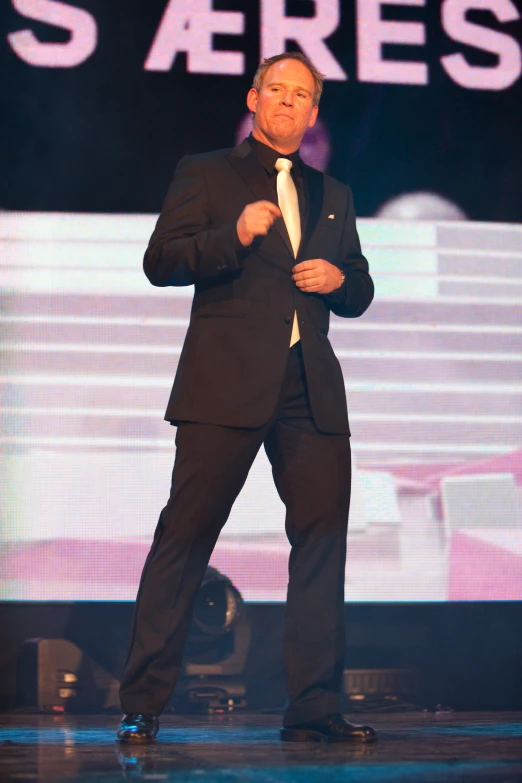 a man in a black suit is doing a stand up dance